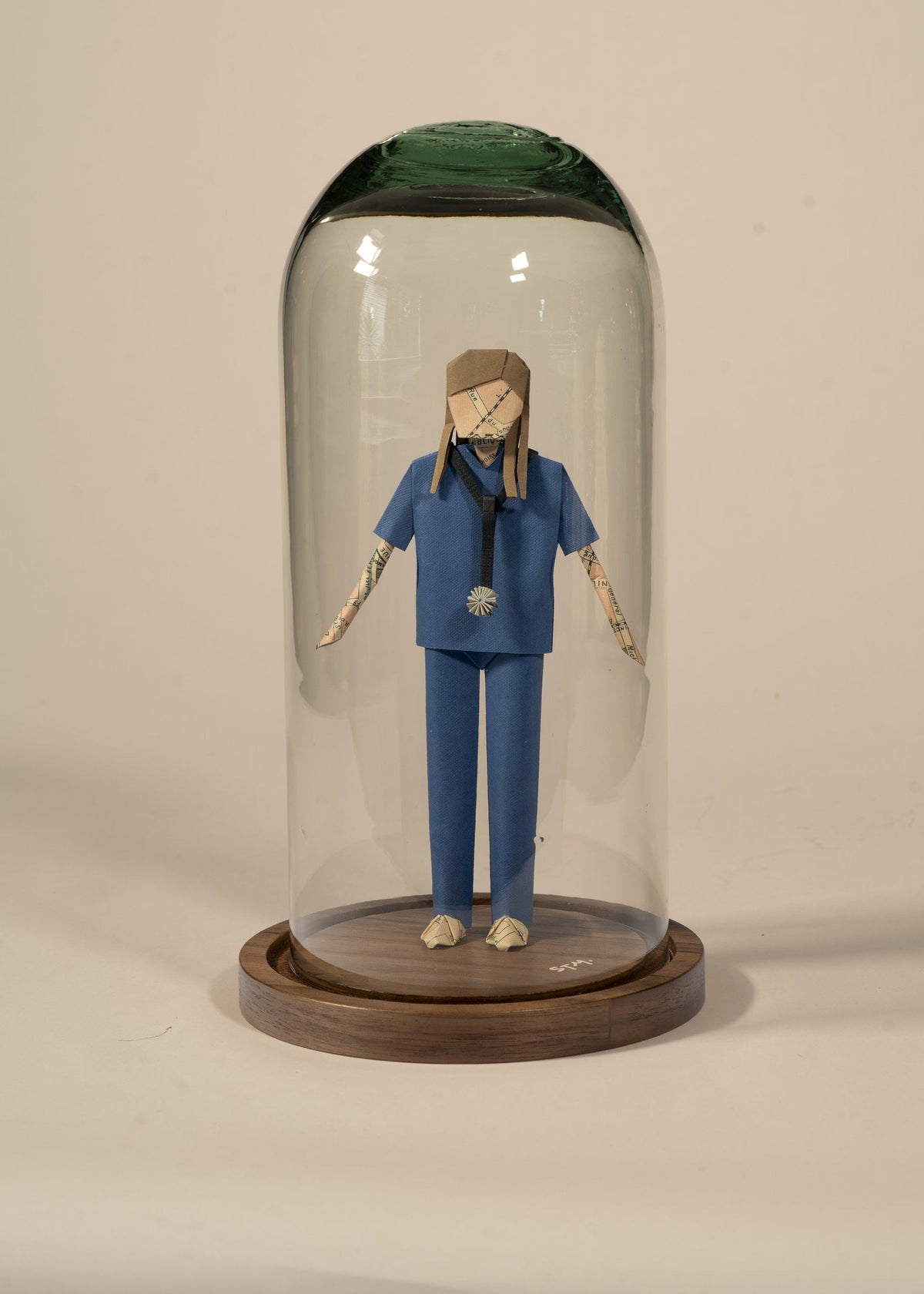Doctor de origami con scrubs azules, en capelo de vidrio sobre base de madera