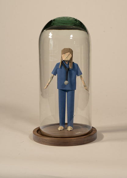 Doctor de origami con scrubs azules, en capelo de vidrio sobre base de madera