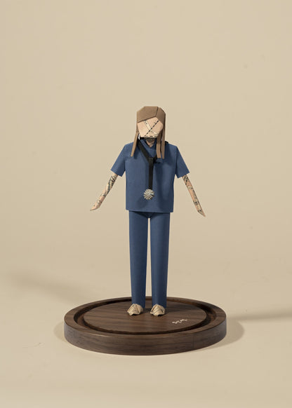 Figura de doctora de origami con scrubs azules y estetoscopio, sobre base de madera