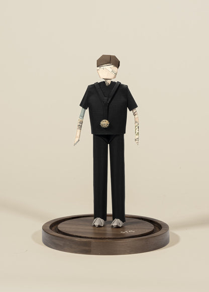 Figura de doctor de origami con scrubs negros, sobre base de madera