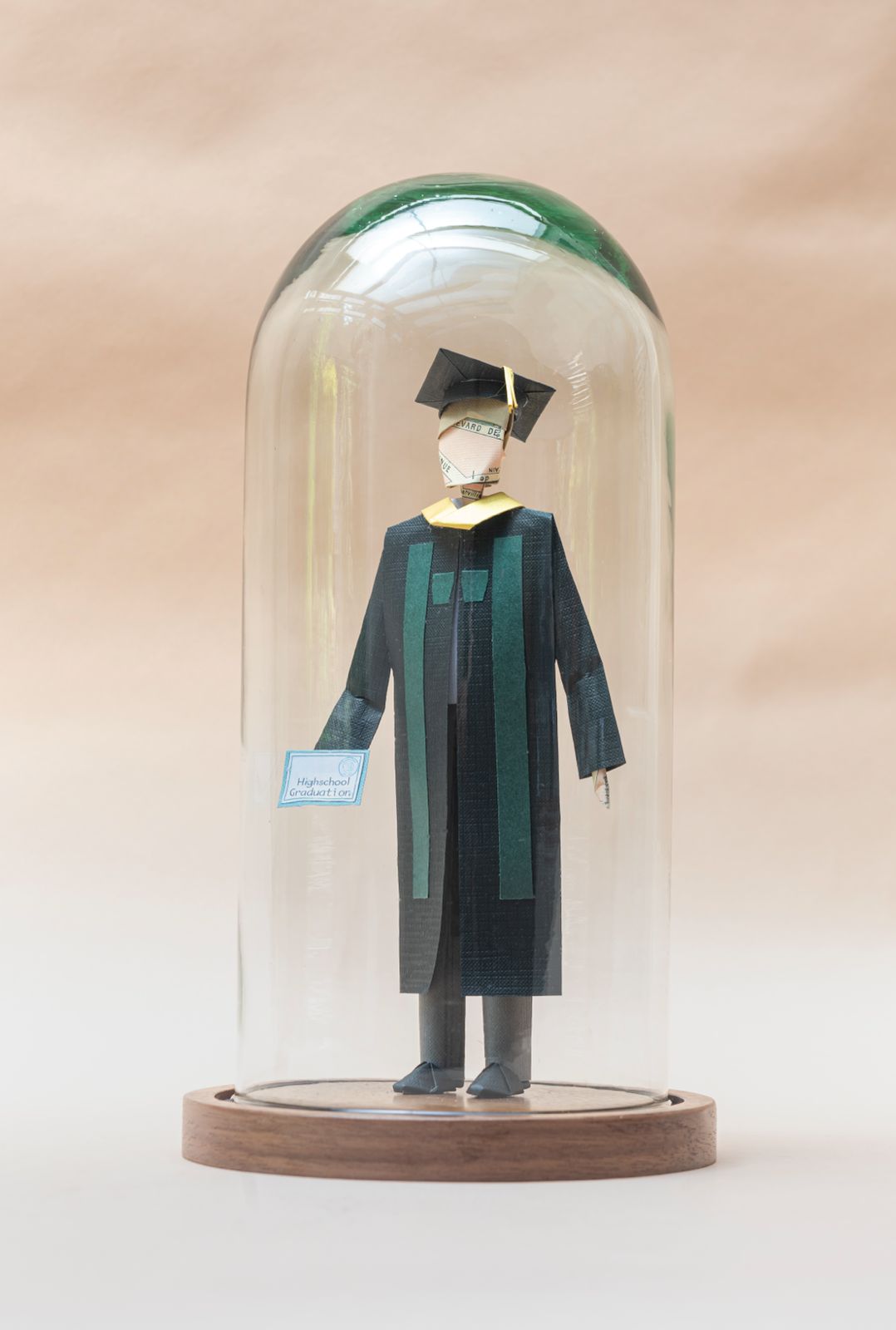 Graduado con toga negra y estola verde, dentro de capelo de vidrio