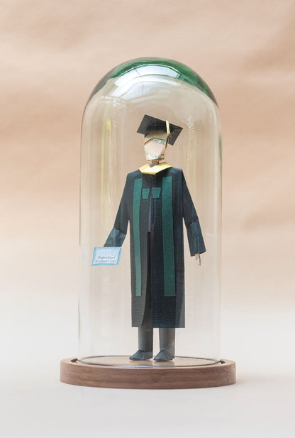 Graduado con toga negra y estola verde, dentro de capelo de vidrio