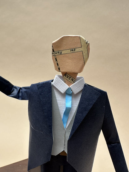 Detalle del novio de papel: traje azul marino, chaleco y corbata celeste