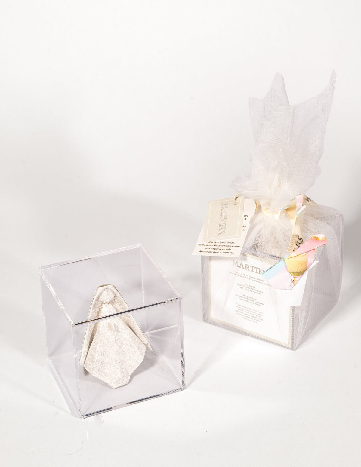 Virgen de origami para bolo en caja de acrílico, junto al bolo ya envuelto con papel de seda y tarjeta