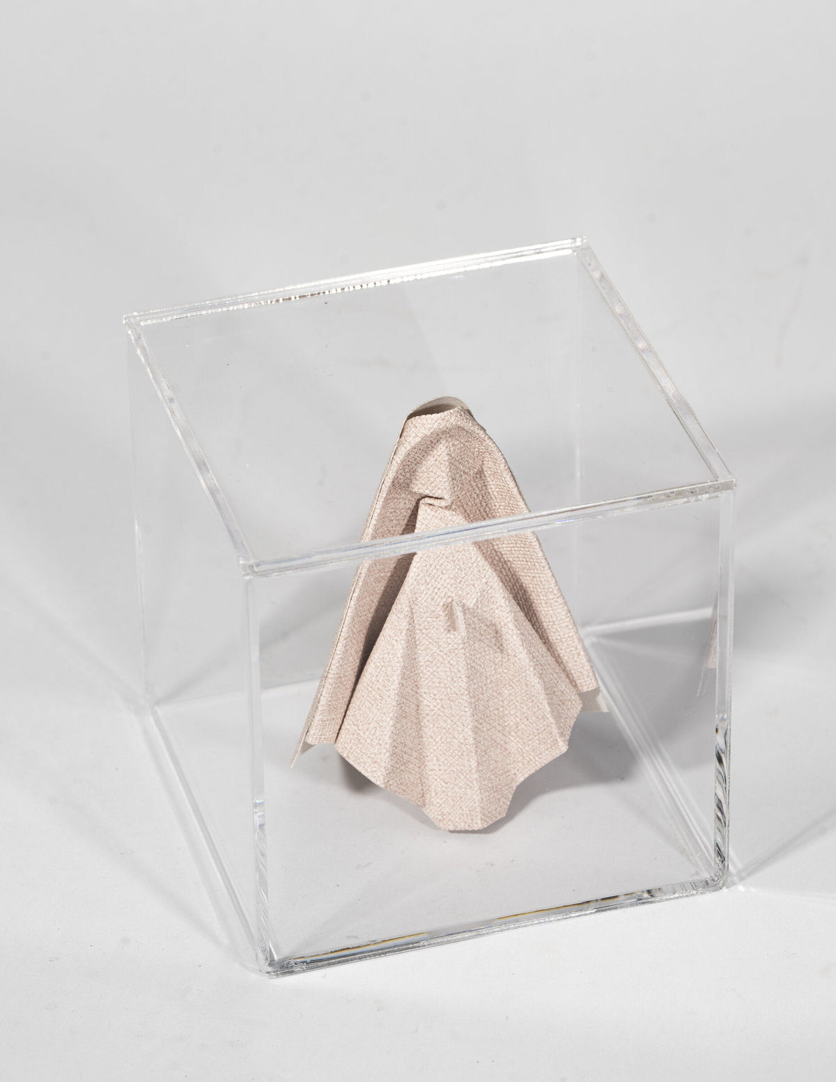 Virgen de origami en papel tapiz rosa, dentro de caja de acrílico, vista de tres cuartos