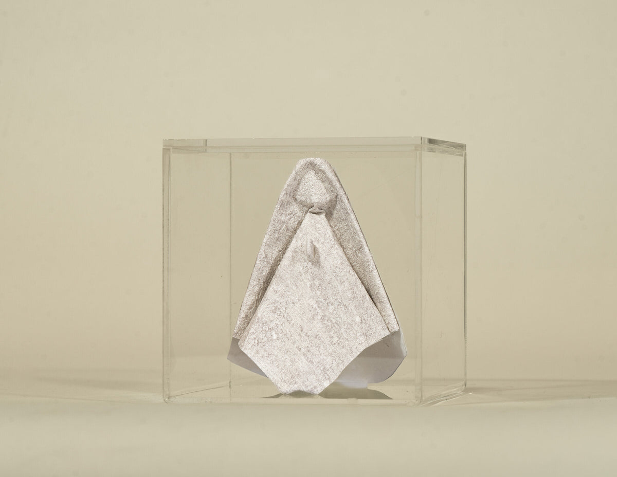 Virgen de origami en papel tapiz claro, dentro de su caja de acrílico